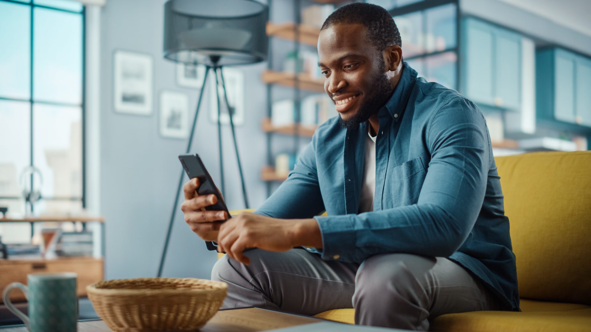 An African American man sits on a yellow device with his mobile device looking at P&A's account management tools.